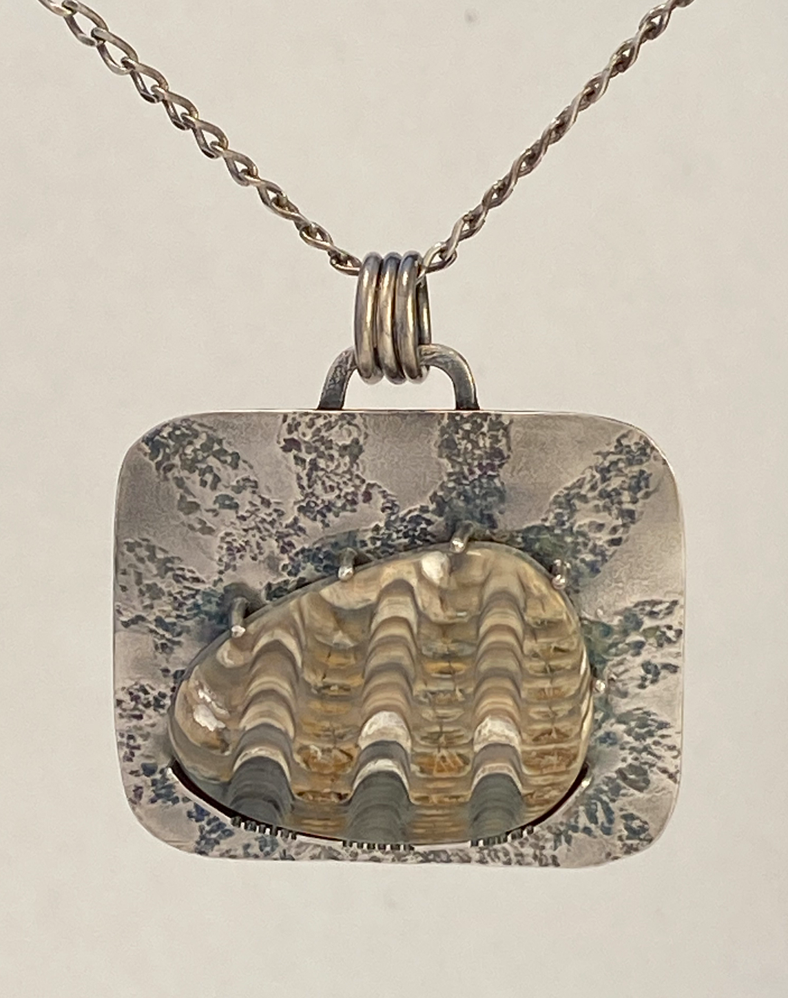 At the heart of this sterling silver piece is beautiful Anadara stone, an ancient fossilized sea shell.  There is a lace pattern pressed into the metal back plate, simulating a sunrise  19" sterling silver chain with a handcrafted clasp. Just over 1” tall and about 1.5” wide.  Style: rustic, boho, funky, organic, earthy yet elegant