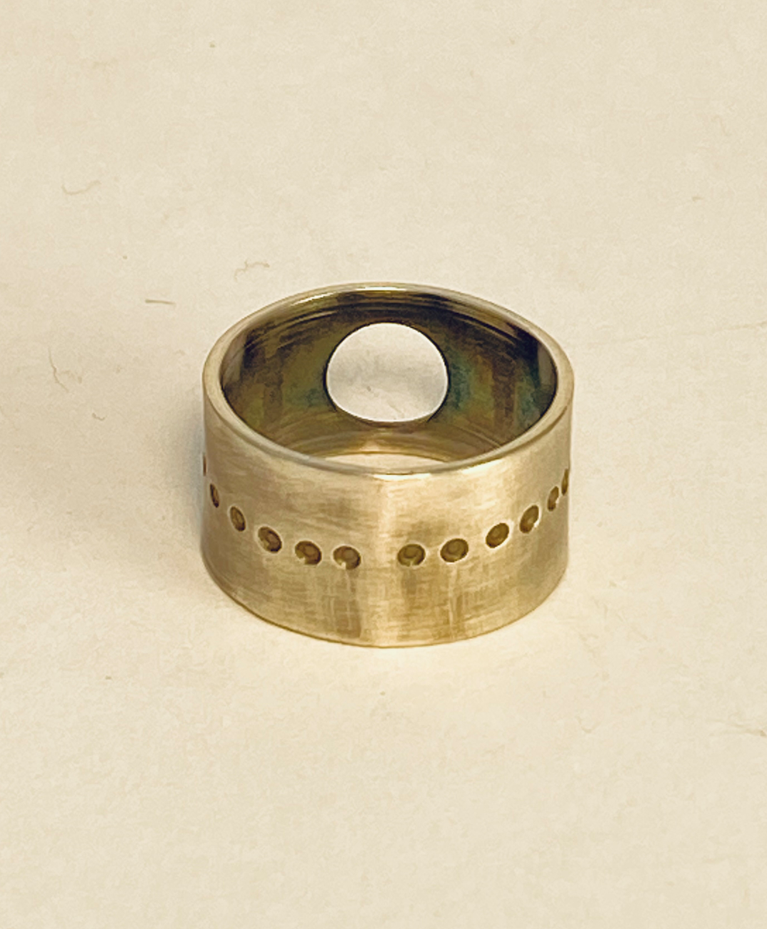 This unique sterling silver band is adorned with round 14k gold embellishments, a circle opening, and a pattern of small circles around the circumference.