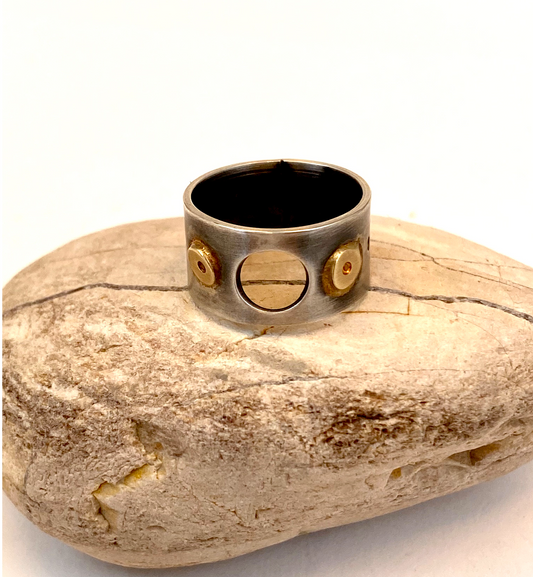 This unique sterling silver band is adorned with round 14k gold embellishments, a circle opening, and a pattern of small circles around the circumference.
