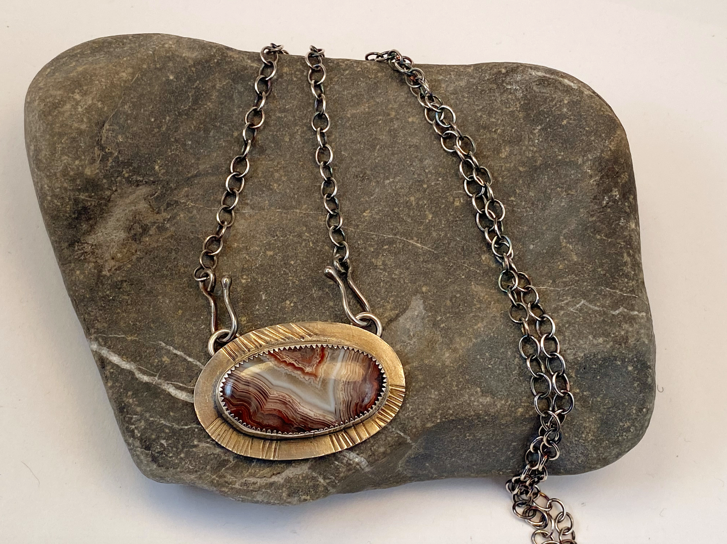 Crazy lace agate with beautiful red, white and gray colors graces this one-of-a-kind necklace.   Set on textured  backplate of sterling silver.  19" sterling silver chain with unique handcrafted clasps that attach in front. Approx. 1” tall 2” wide.  Style: rustic, boho, funky, organic, earthy, natural