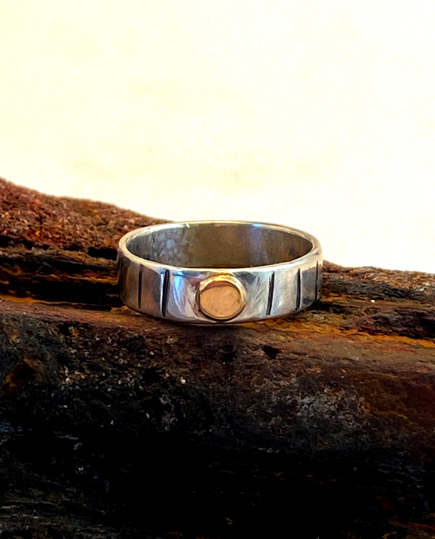      This one-of-a-kind sterling silver ring is adorned with a 14k gold disk and a stamped line pattern around the band.      Ring size 6-14.  Band is 3/16" wide.     Style: rustic, boho, funky, organic, earthy yet elegant