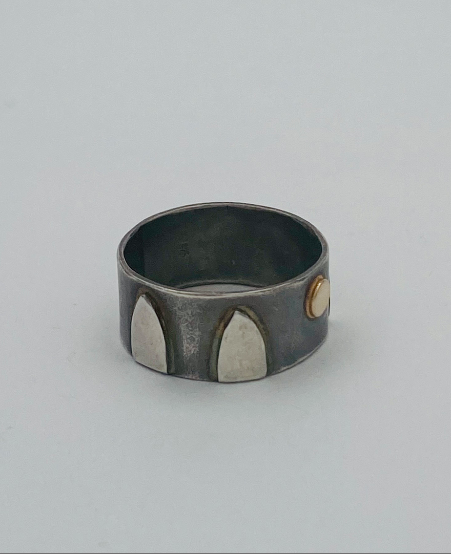 This one-of-a-kind sterling silver band is adorned with arched forms in a pattern around the sides of the ring and one central 14k gold disk.  Background is patinas to dark gray; raised forms are high polish. Ring size 9. 1/3' tall.  Style: rustic, boho, funky, organic, earthy yet elegant