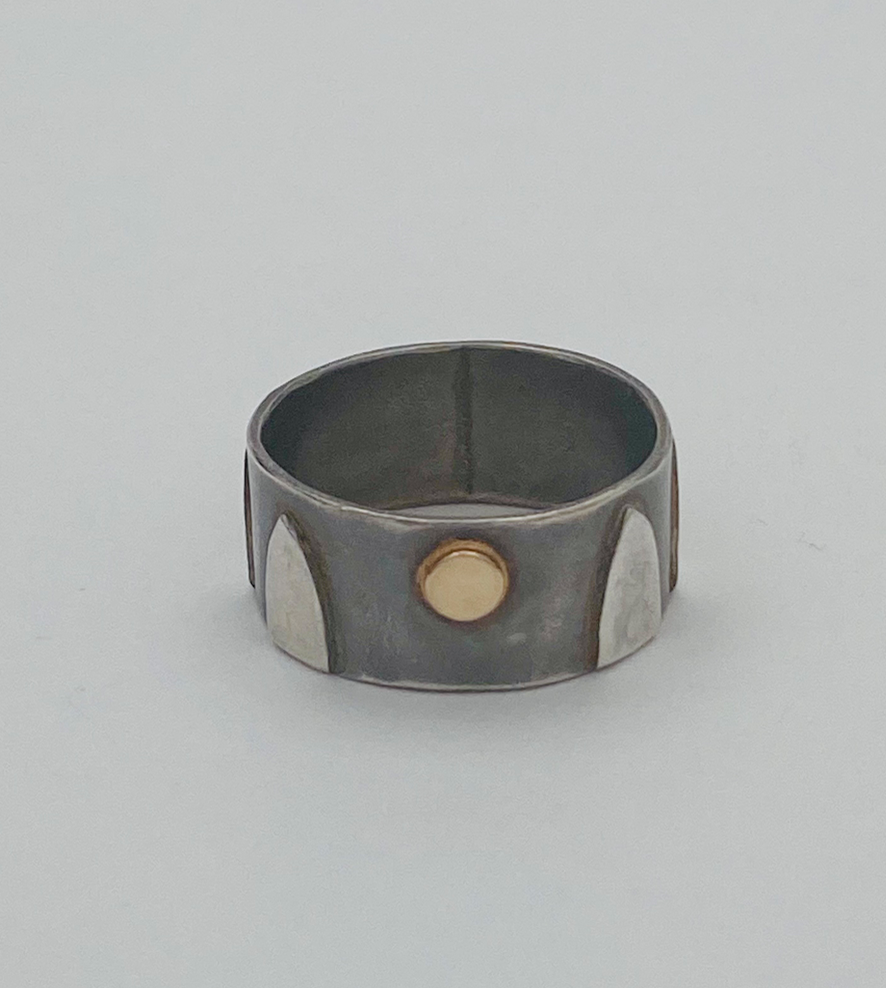 This one-of-a-kind sterling silver band is adorned with arched forms in a pattern around the sides of the ring and one central 14k gold disk.  Background is patinas to dark gray; raised forms are high polish. Ring size 9. 1/3' tall.  Style: rustic, boho, funky, organic, earthy yet elegant