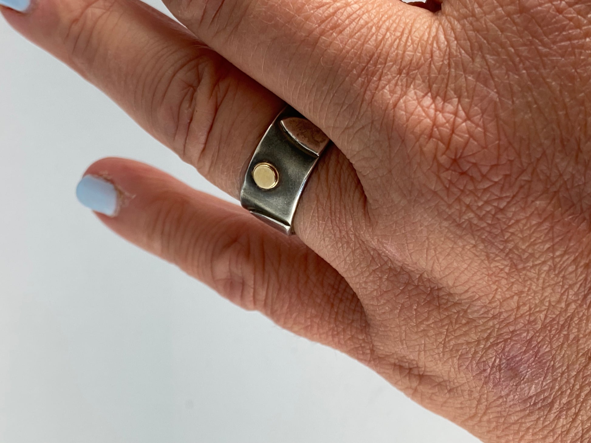 This one-of-a-kind sterling silver band is adorned with arched forms in a pattern around the sides of the ring and one central 14k gold disk. Background is patinas to dark gray; raised forms are high polish. Ring size 9. 1/3' tall. Style: rustic, boho, funky, organic, earthy yet elegant